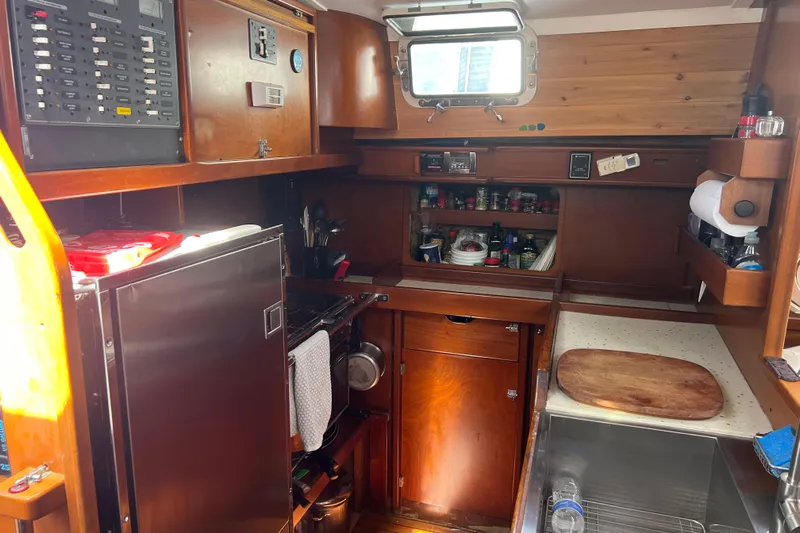 Hobo Tiempo Yacht Photos Pics Compact kitchen in a 1986 Amel Mango sailboat, featuring wooden cabinetry and essential appliances.