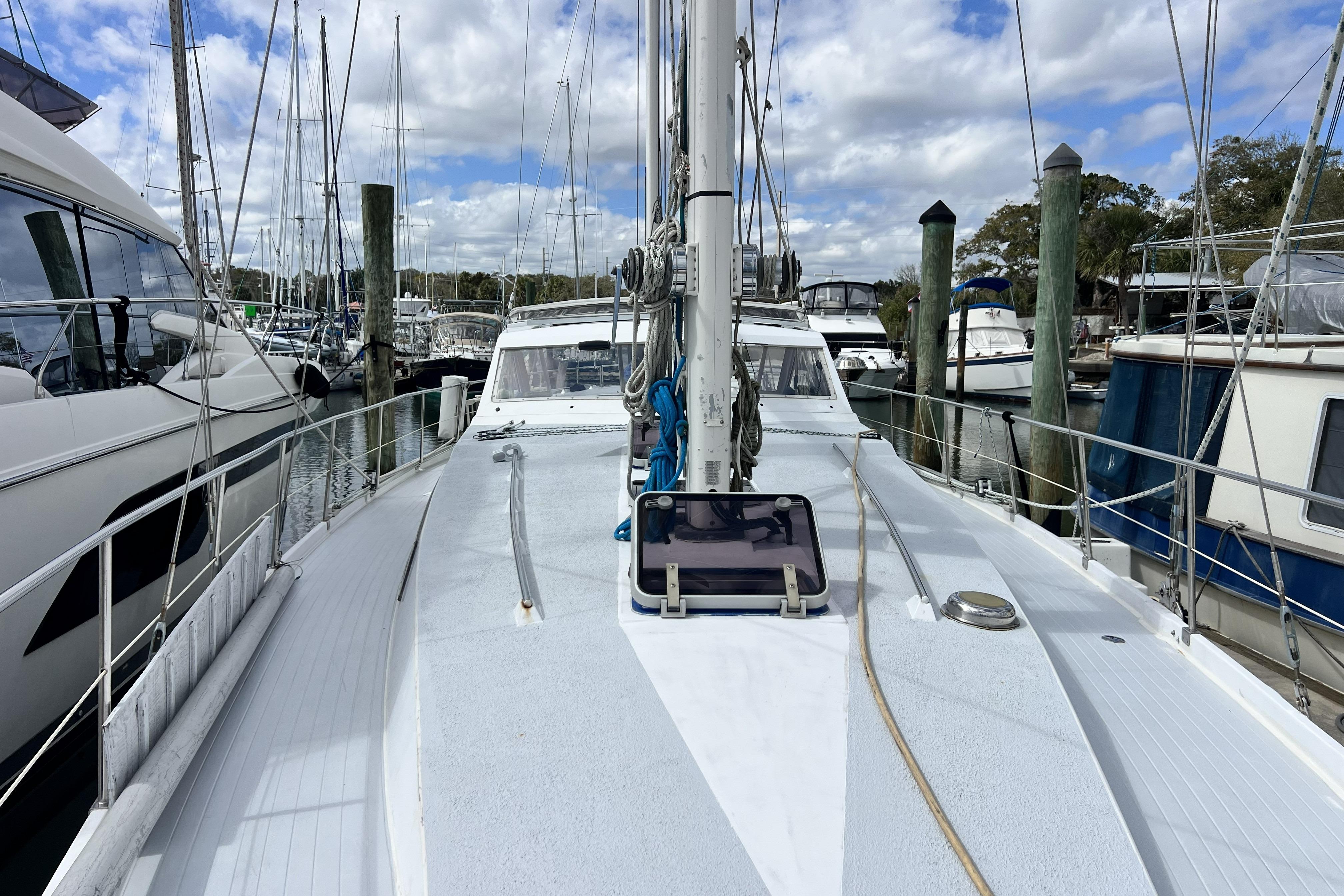 1986 Amel Mango sailboat docked at marina, surrounded by other boats under a cloudy sky.