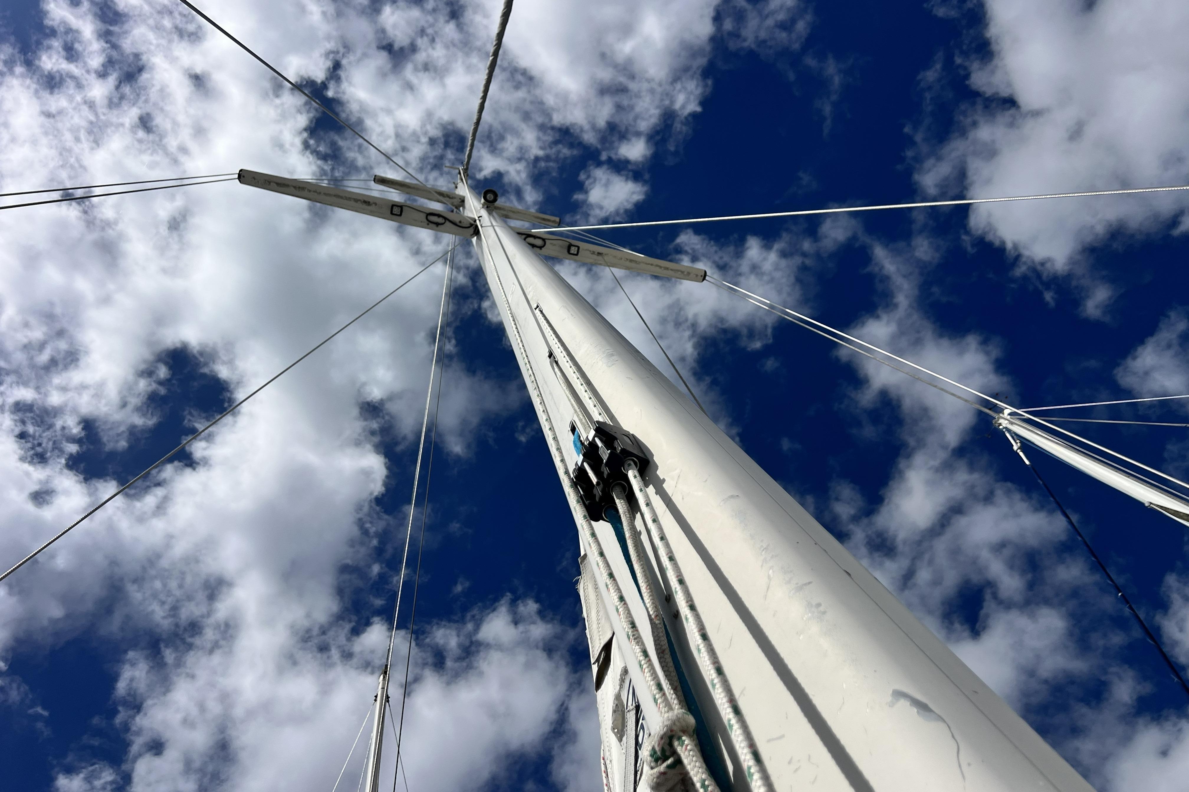 Sailboat mast of 1986 Amel Mango against a cloudy blue sky.