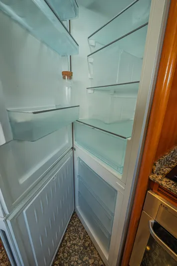 Isabella K Yacht Photos Pics Empty refrigerator inside 2002 Astondoa 72 GLX yacht, featuring glass shelves and wooden cabinetry.