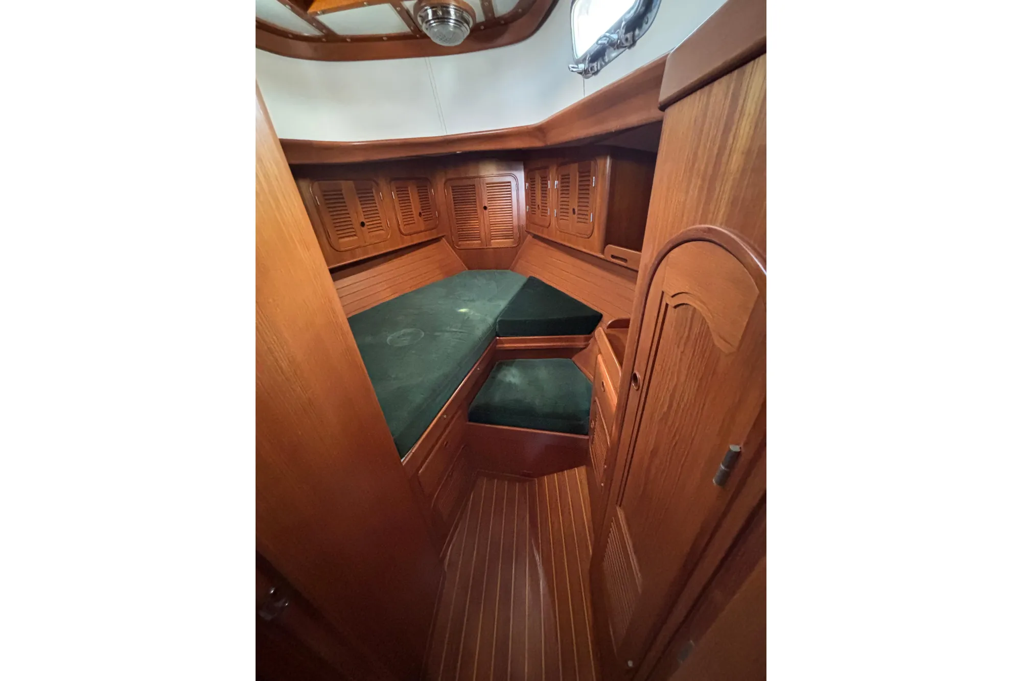 Cozy cabin interior of 1985 Mason 33 sailboat with wooden finish and green cushions.