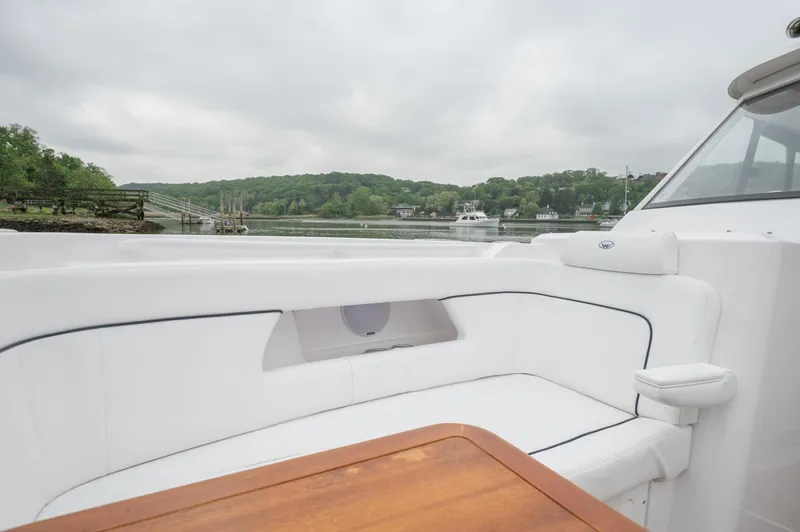 Even Flow Yacht Photos Pics 2021 Southport 33 DC boat with white seating and wooden table, docked by a scenic riverside.