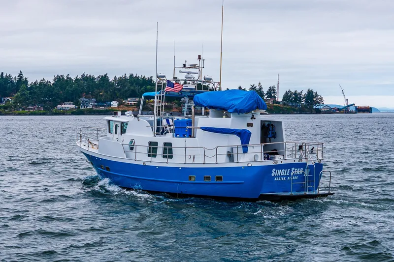 Single Star Yacht Photos Pics Blue and white 1978 Hidden Harbor Custom Trawler on water, with American flag, near forested shoreline.