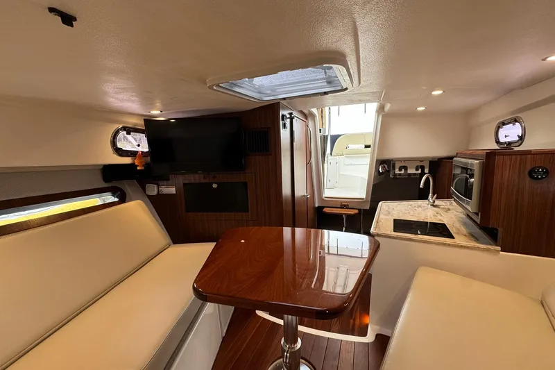  Yacht Photos Pics 2018 Pursuit OS 325 Offshore cabin interior with seating, table, kitchenette, and TV.