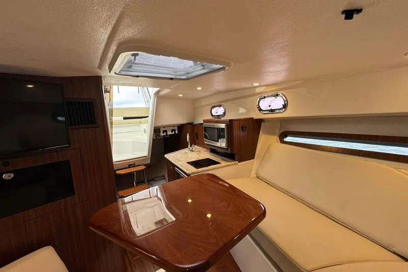  Yacht Photos Pics 2018 Pursuit OS 325 Offshore cabin interior with seating, table, and kitchenette.
