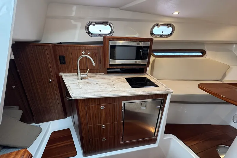  Yacht Photos Pics 2018 Pursuit OS 325 Offshore boat interior with kitchenette, featuring wood cabinetry and modern appliances.