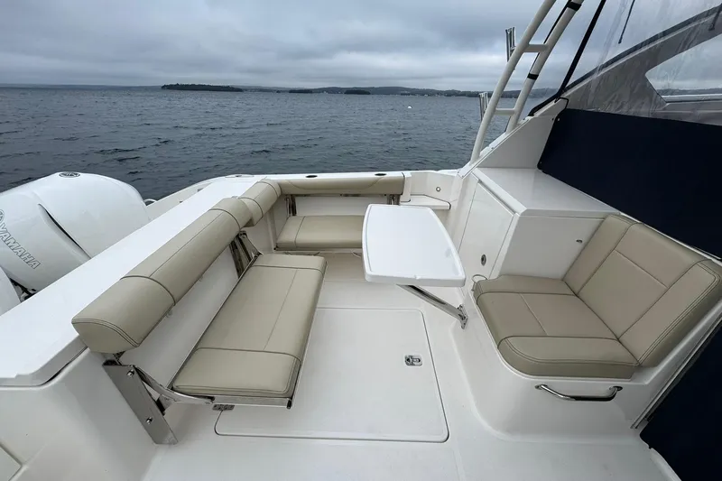  Yacht Photos Pics 2018 Pursuit OS 325 Offshore boat interior with beige seating and table on a cloudy day.