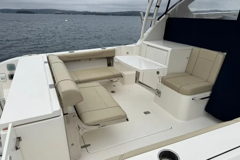  Yacht Photos Pics 2018 Pursuit OS 325 Offshore boat interior with beige seating and table on a calm lake.