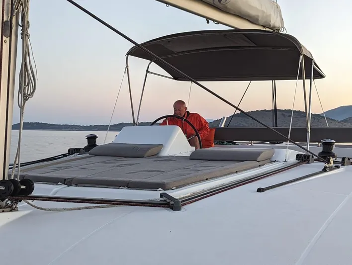  Yacht Photos Pics Man steering a 2014 Lagoon 450 catamaran at sunset on calm waters.
