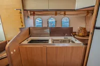 Compact kitchen area in a 2005 Astondoa 53 Open yacht with stove, sink, and porthole windows.