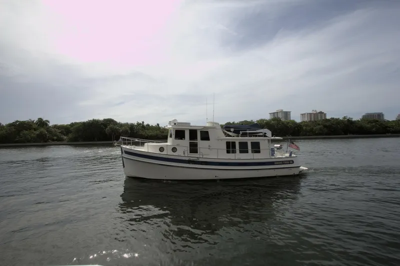 Hercules Yacht Photos Pics Nordic Tug 42 Millennium 2000 cruising on a calm river with cityscape background.