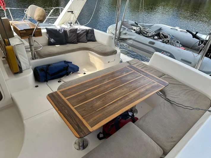 Bat Ha Yam Yacht Photos Pics Leopard 47 catamaran cockpit with wooden table, cushioned seating, and inflatable dinghy, 2001 model.