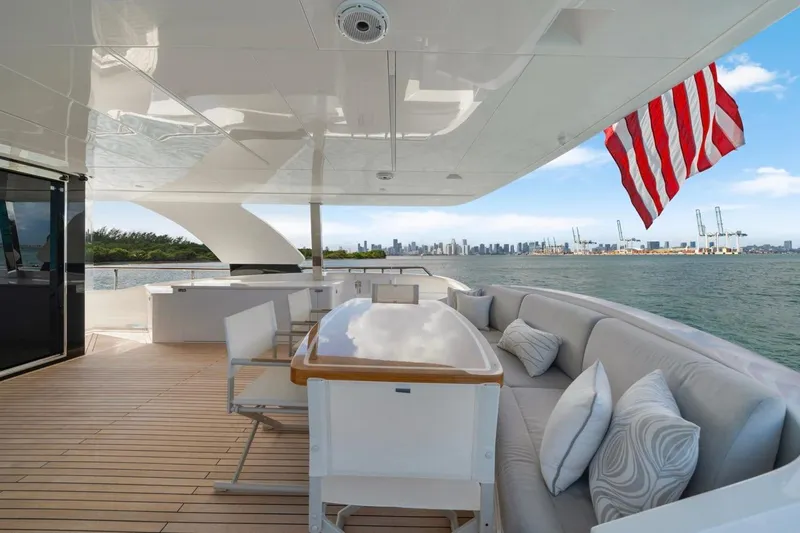 Valiant Yacht Photos Pics Luxurious Horizon E81 yacht deck with seating, table, and American flag, overlooking city skyline.