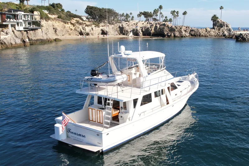 Treasure Yacht Photos Pics 1997 Offshore Yachts 48 Sedan cruising near rocky coastline with palm trees.