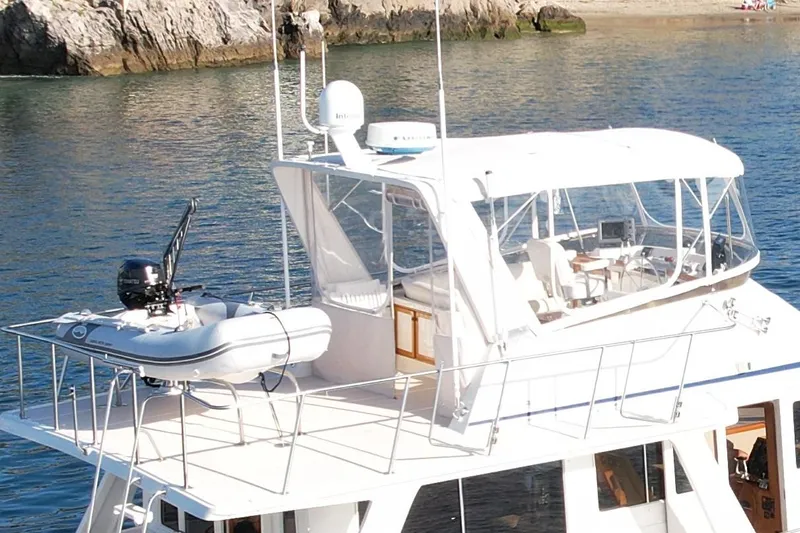 Treasure Yacht Photos Pics 1997 Offshore Yachts 48 Sedan with dinghy on deck, anchored near rocky shoreline.