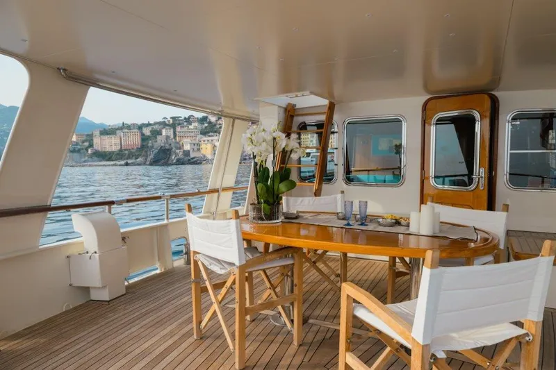 Yona Yacht Photos Pics Luxurious 1981 Vripack Doggersbank 20 yacht deck with elegant dining setup and scenic coastal view.