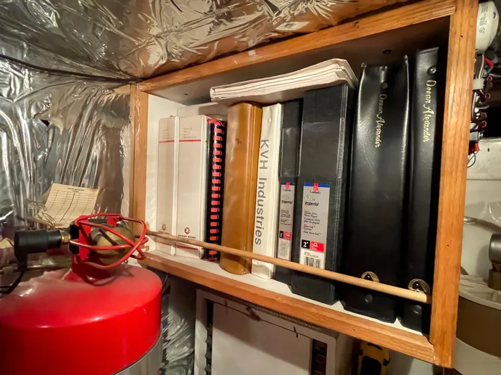 Wind Star Yacht Photos Pics Shelf with manuals and binders for Ocean Alexander 520 Pilothouse, 1993, in a metallic-walled space.