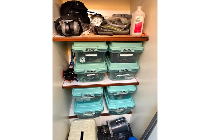 Traveller Yacht Photos Pics Storage shelves with labeled Hefty bins, headphones, and cleaning supplies on a Jefferson 52 Rivanna Cockpit MY.