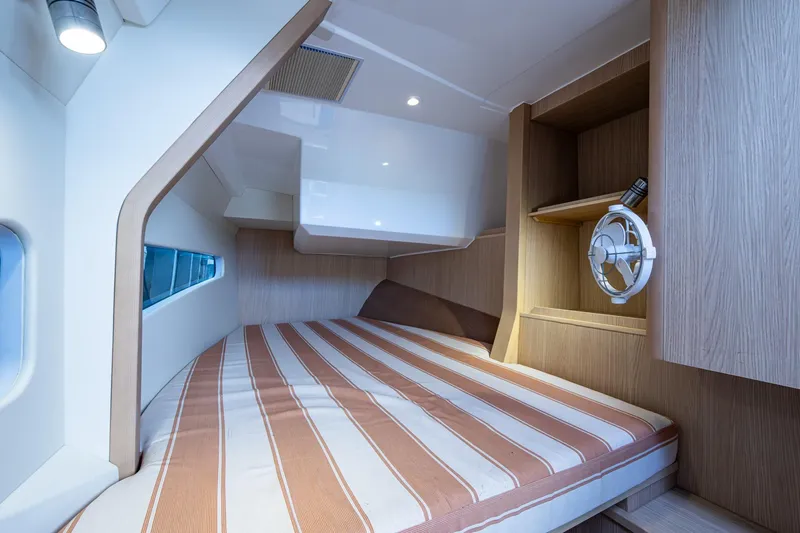  Yacht Photos Pics 2023 Aquila 32 Power Cat cabin with striped bedding and wooden interior design.