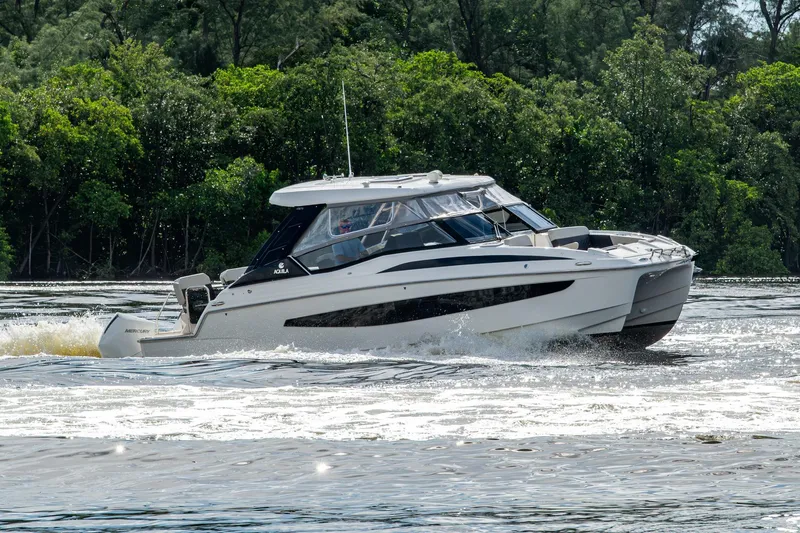  Yacht Photos Pics 2023 Aquila 32 Power Cat cruising on a river with lush green trees in the background.