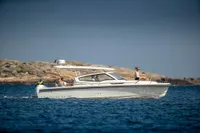 2023 Nimbus W9 boat cruising on blue water near rocky coastline.