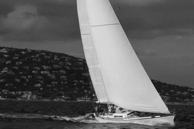 Django Too Yacht Photos Pics Sailing yacht THEHARD SLOOP 83, 1991, gliding on water with hillside backdrop.