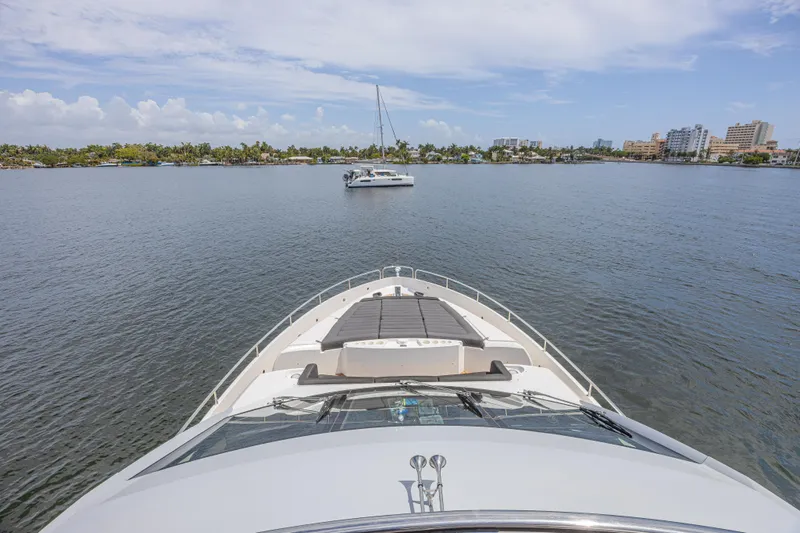 Dirty Dawg Yacht Photos Pics Bow view of 2017 Sunseeker 75 Yacht on calm waters, distant cityscape.