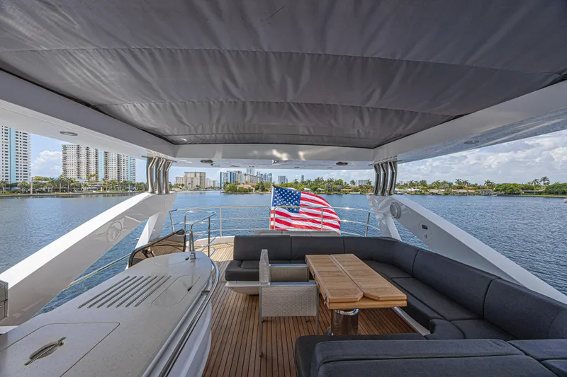 Dirty Dawg Yacht Photos Pics Luxurious 2017 Sunseeker 75 Yacht deck with seating, table, and American flag, overlooking waterfront cityscape.