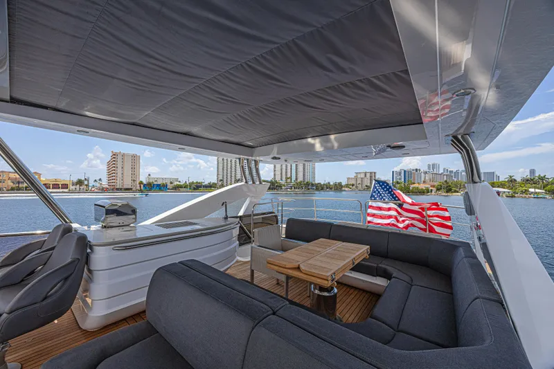 Dirty Dawg Yacht Photos Pics Luxurious 2017 Sunseeker 75 Yacht deck with seating, table, and American flag, overlooking waterfront cityscape.