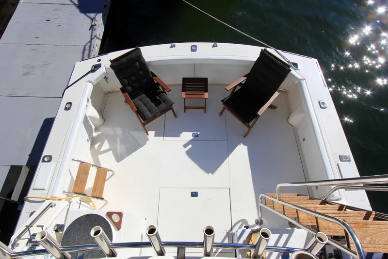 La Dorada Yacht Photos Pics Bertram 35 Flybridge 1980 boat deck with chairs and table, docked by sparkling water.