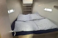 Cozy cabin interior of 2023 Hanse 388 yacht with striped bedding and natural light.
