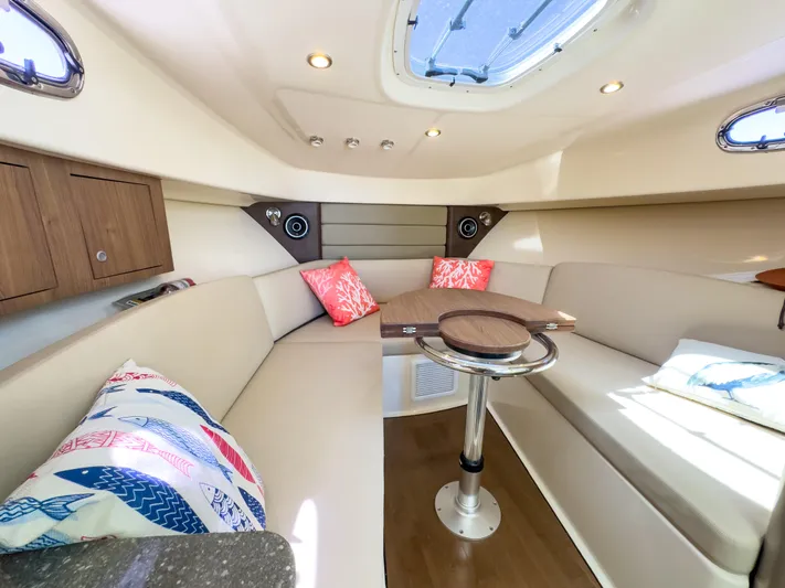 Pearl Yacht Photos Pics 2018 Boston Whaler 315 Conquest cabin interior with seating, table, and decorative pillows.