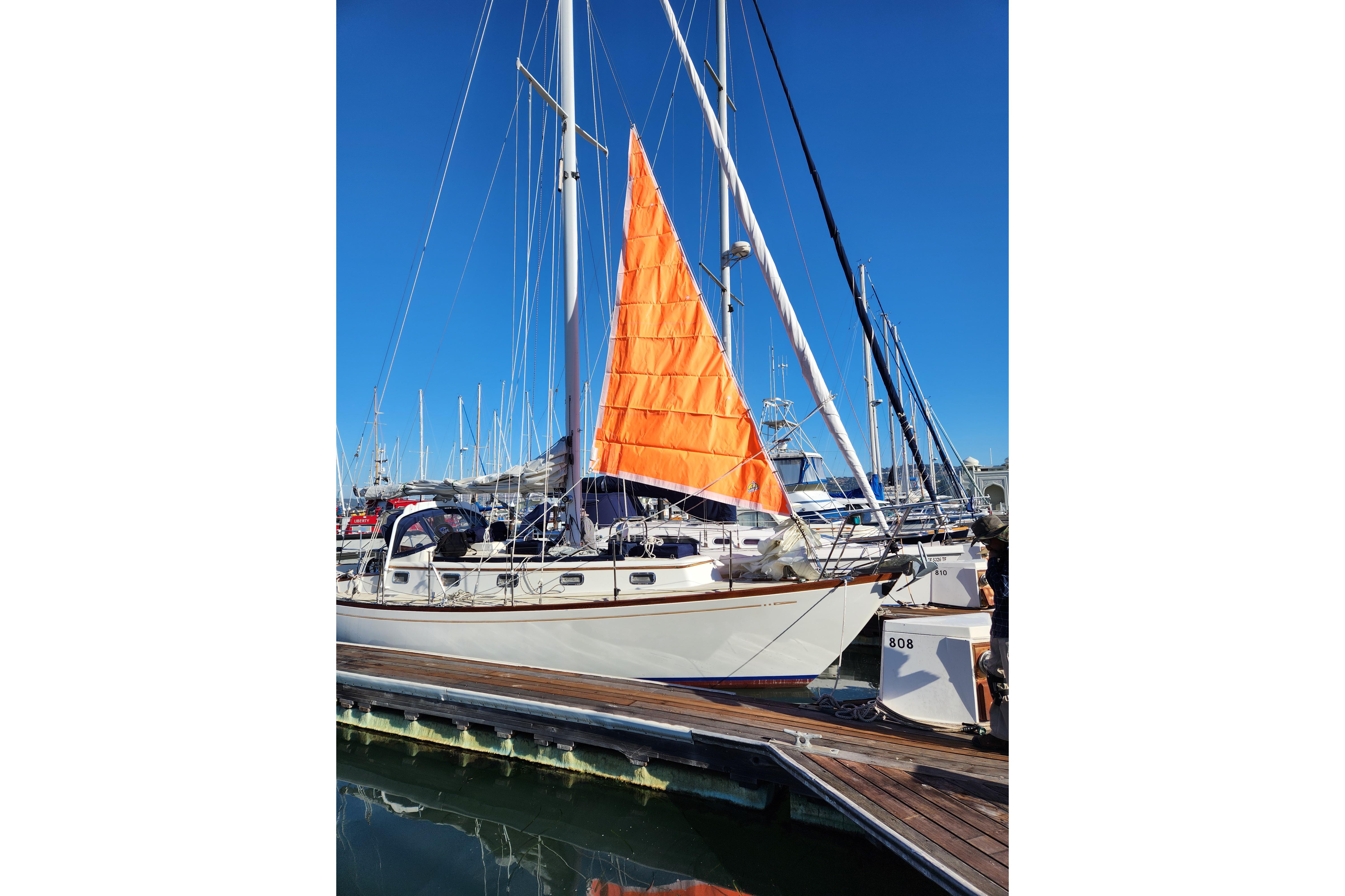 Sailboat Mason 33, 1985 model, docked with vibrant orange sail against clear blue sky.
