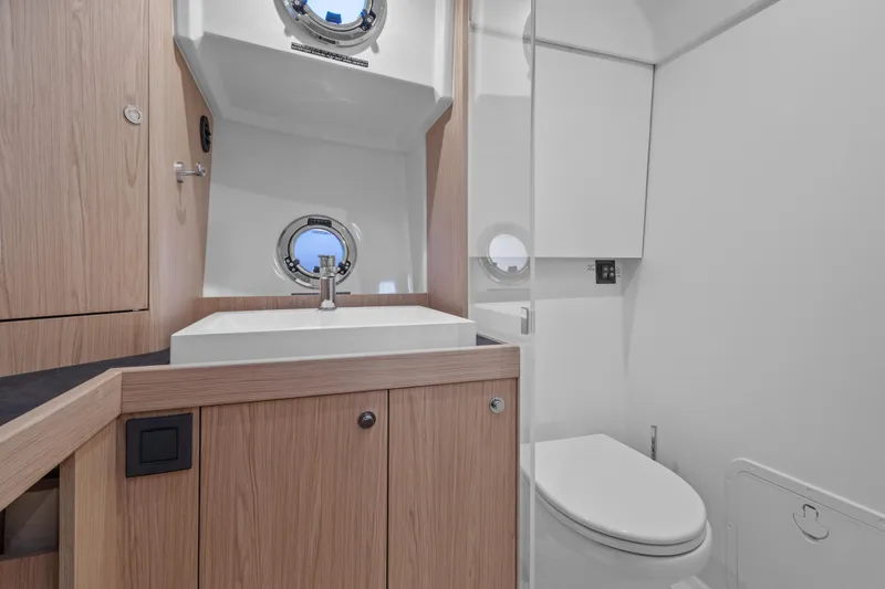 Unfiltered Yacht Photos Pics Modern bathroom in 2023 Beneteau Swift Trawler 35, featuring sleek wood cabinetry and porthole window.