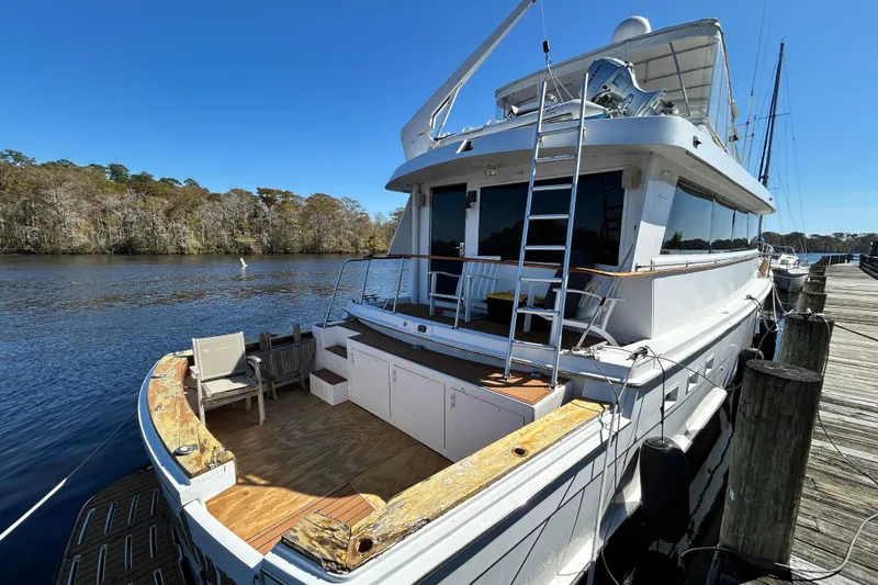 Nother Venture Yacht Photos Pics 1989 Hatteras 78 CPMY yacht docked by a serene river under a clear blue sky.