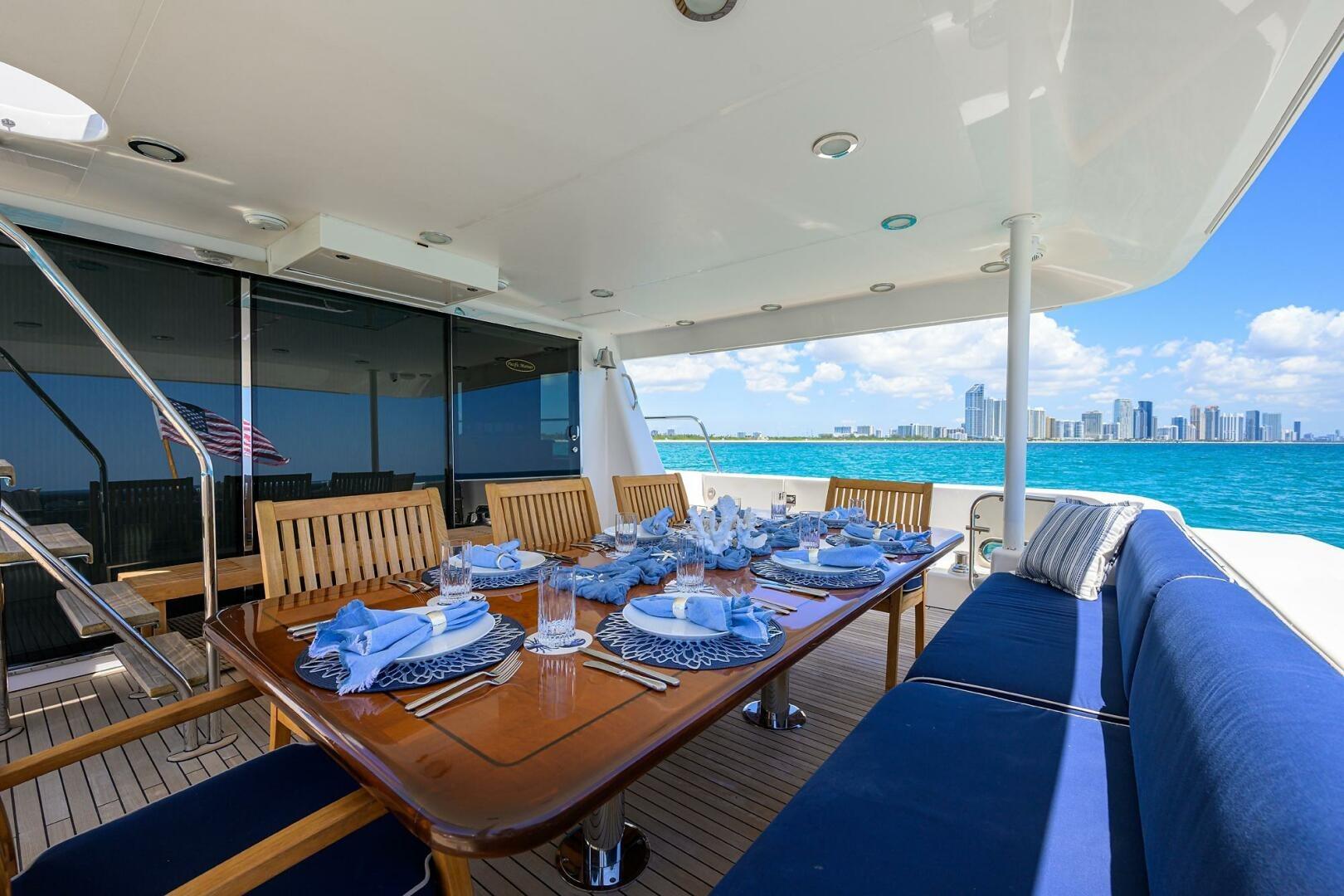 Luxurious dining setup on 2005 Pacific Mariner 85 yacht, overlooking ocean and city skyline.