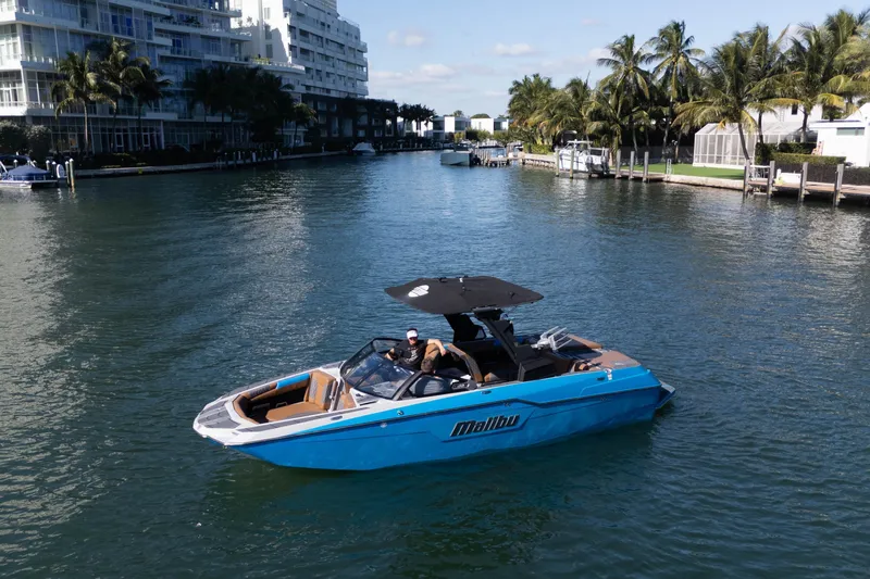  Yacht Photos Pics 2020 Malibu M240 boat cruising on a scenic waterway with palm trees and buildings.