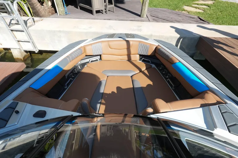  Yacht Photos Pics 2020 Malibu M240 boat interior with brown and blue seating, docked by a wooden deck.