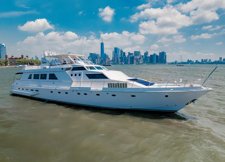 Justine Yacht Photos Pics Luxurious 1987 Guy Couach 97 yacht cruising near a city skyline under a blue sky.