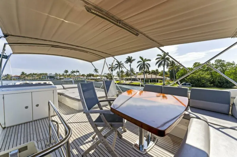 Never Enough Yacht Photos Pics Prestige 550 Flybridge 2013 yacht deck with seating, table, and canopy, surrounded by palm trees.