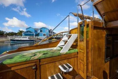 Flamingo Yacht Photos Pics 1950 Monk Pilothouse boat with wooden deck, docked near blue houses under a clear sky.
