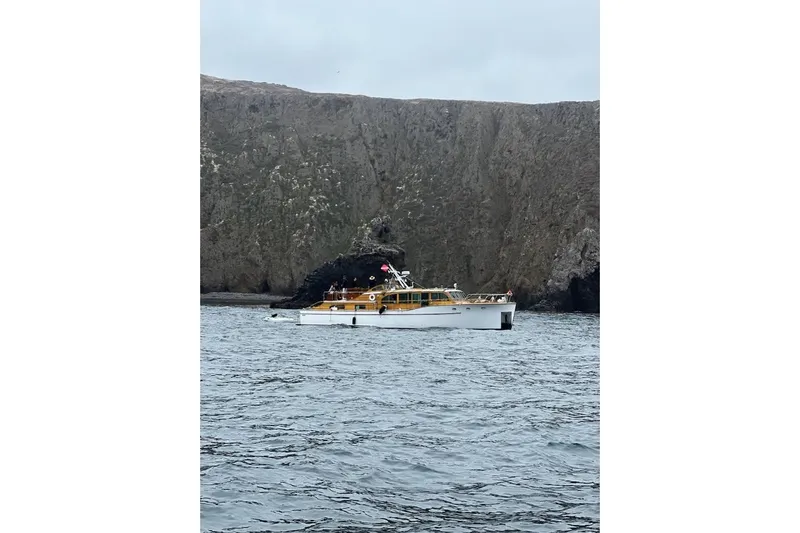 Flamingo Yacht Photos Pics 1950 Monk Pilothouse boat on water near rocky cliffs.