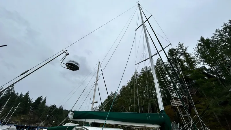  Yacht Photos Pics Sailboat with tall mast, green cover, docked near forested shoreline, overcast sky. Custom Seawing-Atkins 2002.