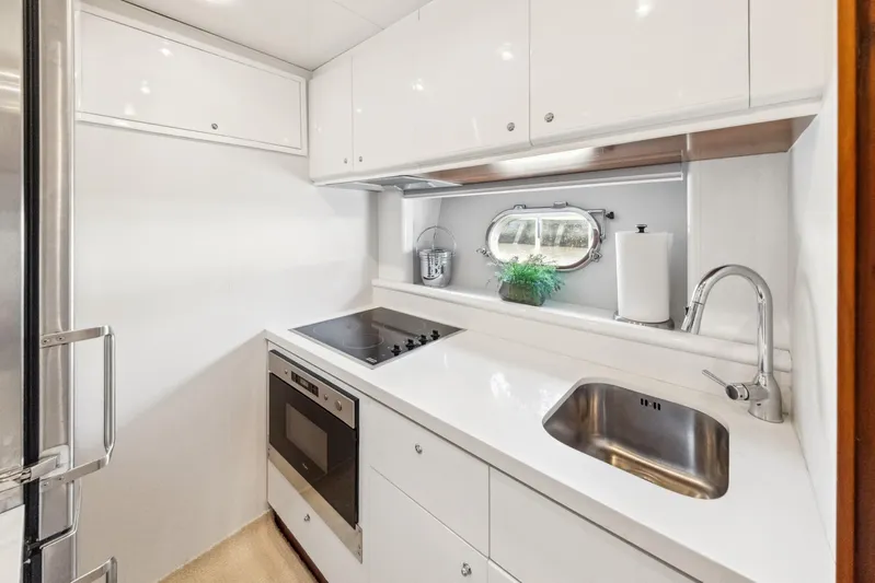 Alchemy Yacht Photos Pics Compact yacht kitchen with modern appliances, white cabinetry, and a small porthole window. Baia PANTHER 80, 2003.