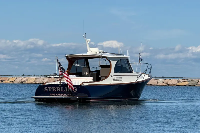 Sterling Yacht Photos Pics 2024 Hinckley Picnic Boat 40 S cruising near rocky shoreline under blue sky.