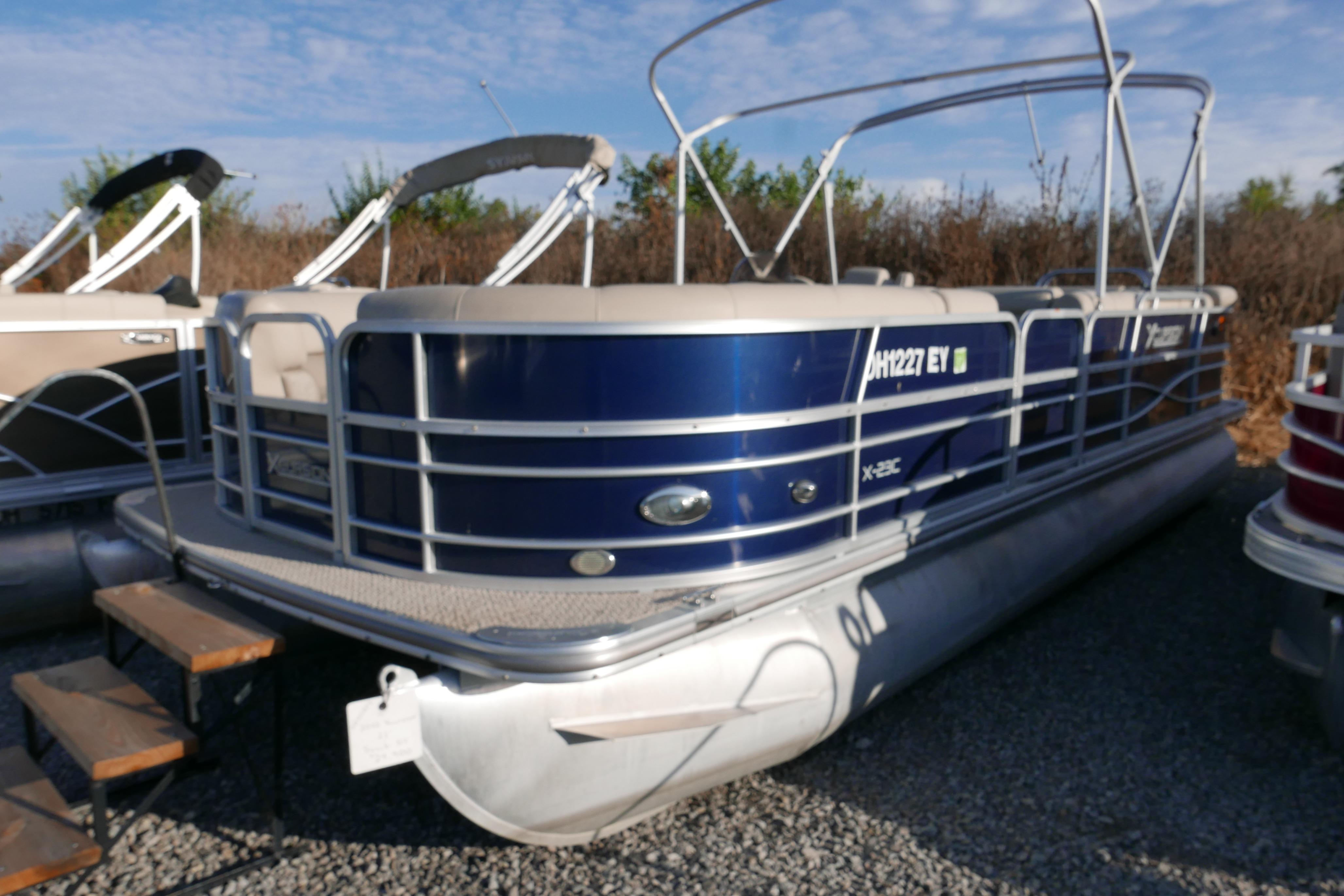2012 Xcusrion x2312 pontoon boat with blue exterior, docked on gravel.