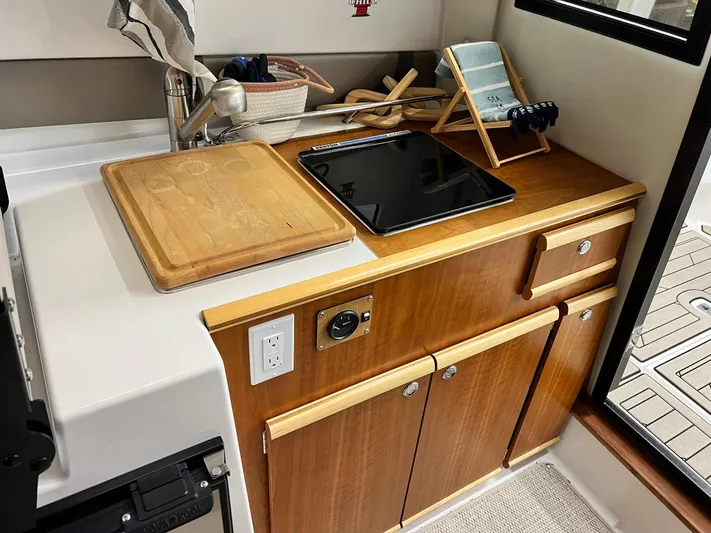  Yacht Photos Pics 2022 Cutwater C-24 Coupe kitchen area with wooden cabinetry and modern appliances.