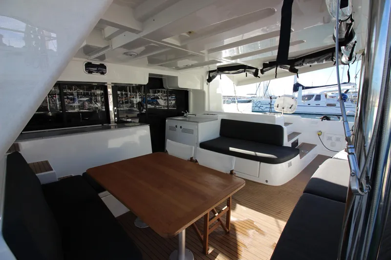 Alma De Sur Yacht Photos Pics Spacious Lagoon 46 catamaran cockpit with seating, table, and marina view, 2021 model.