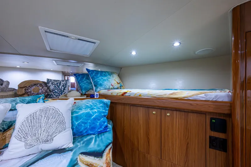 Adrian & Leidiana Yacht Photos Pics Cozy cabin interior of 2005 Viking 61 yacht with nautical-themed bedding and wooden cabinetry.