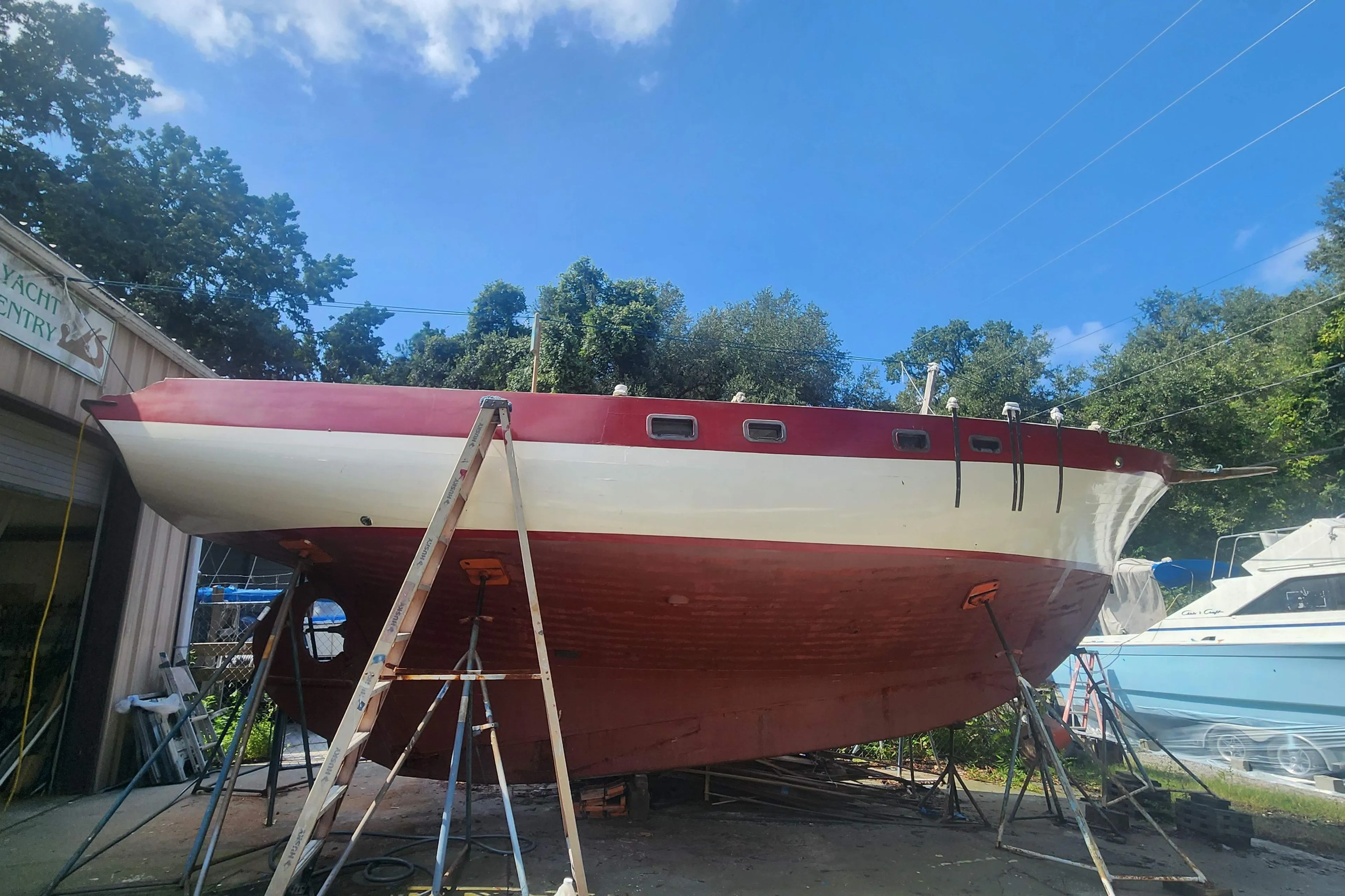 1959 Geerd Hendel Raised-Deck Cutter sailboat on stands, undergoing maintenance outdoors.